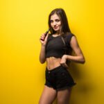 Young woman with vape smoke gadget standing isolated on yellow background